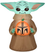 Halloween inflatable decoration shaped like baby Grogu from the show The Mandalorian. He's holding a small pumpkin that's been carved to look like a Mandalorian helmet.
