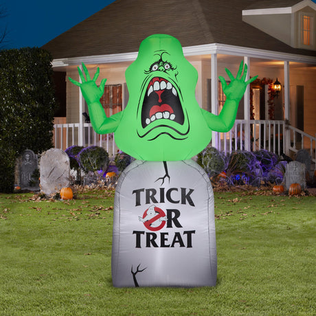 Inflatable Halloween decoration shaped like Slimer, the green ghost from the movie Ghostbusters. He appears to be jumping out from a tombstone that reads "Trick or Treat" and features the Ghostbusters logo.