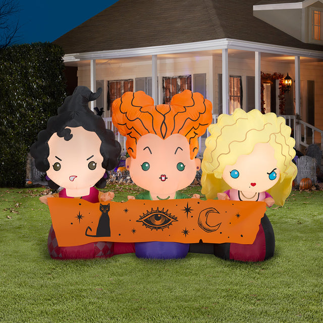 Halloween inflatable decoration designed to look like the three Sanderson sisters from the movie Hocus Pocus. They're all wearing their iconic witch outfits and holding a scroll with a cat, an eye and a crescent moon on it.