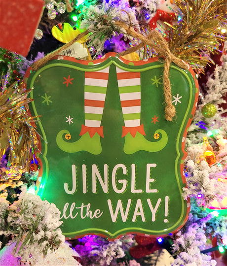 Christmas sign hanging from a jute rope on a Christmas tree with other ornaments and tinsel.