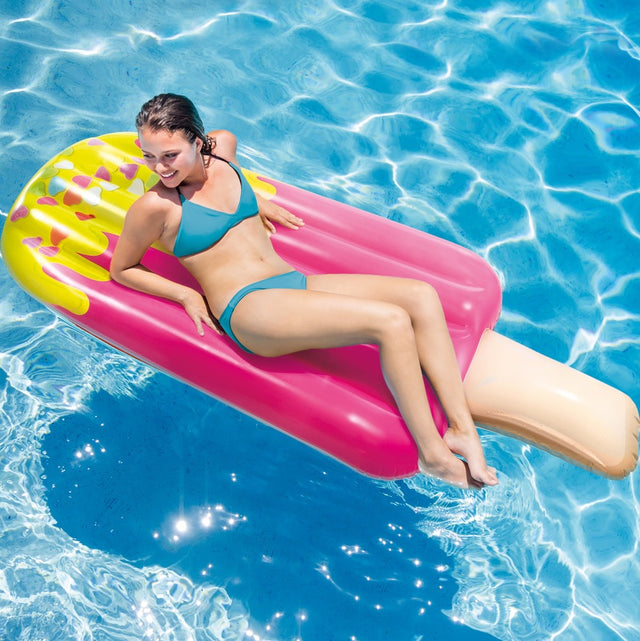 Inflatable pool float shaped like a pink popsicle. The tip of the popsicle looks like it's dipped in yellow frosting with heart shaped sprinkles on it.