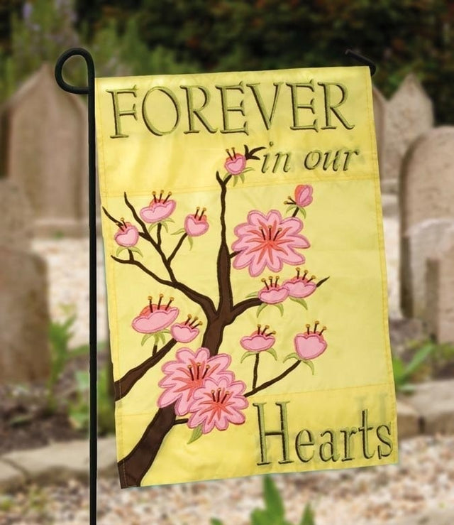 A yellow flag consisting of a cartoon-looking cherry blossom tree and reads "Forever in our Hearts"