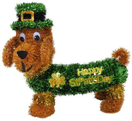 Tabletop decoration made out of shiny tinsel. It's shaped like a light brown Dachshund dog. The dog is wearing a green top hat with a gold buckle on it. He's also wearing a green and gold sweater that reads "HAPPY ST. PAT'S DAY" and has a holographic, gold shamrock.