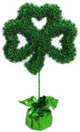 Tinsel tabletop decoration shaped like a shamrock. There's a weighted base covered in shiny, green tinsel.