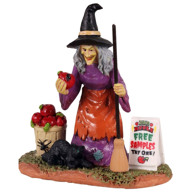 Polyresin figurine for a Lemax display. Designed to look like an old witch offering apples. There's a black cat standing in front of her and a sign that reads "BAD APPLE: FREE SAMPLES. TRY ONE!"