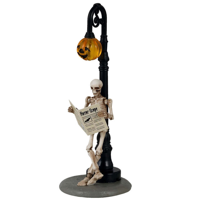 Plastic figurine for a Lemax Spooky Town display. Designed to look like a skeleton leaning up against a lamppost, reading a newspaper. The light on the lamppost is shaped like a jack-o-lantern.