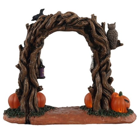 Plastic village accessory for a Lemax Spooky Town display. Designed to look like an arch made of branches. There are skulls and crows and an owl perched on it. There are two skeletons inside the arch that are holding lights. There are four jack-o-lanterns at the base.