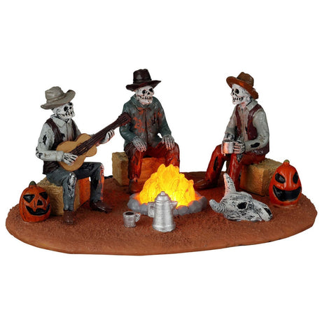 Plastic village accent for a Lemax display. Designed to look like three skeletons sitting around a campfire. They're sitting on bales of hay. There are carved pumpkins and an animal skull on the ground. All three skeletons are wearing cowboy hats and wearing ratty, old clothes. One skeleton is playing the guitar.