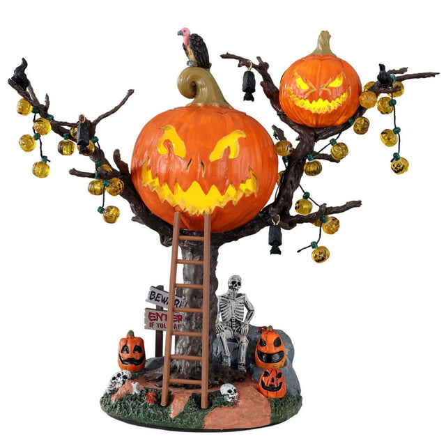 Polyresin village accent for a Lemax display. Designed to look like a treehouse made out of carved pumpkins. There are pumpkin lights, bats and black crows hanging from the branches. There's a vulture on the roof and a ladder leaning against the tree. There's a skeleton sitting underneath the treehouse among skulls, pumpkins and signs reading "BEWARE!" and "ENTER IF YOU DARE!"