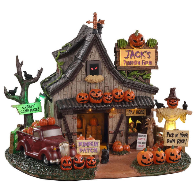 Polyresin building for a Lemax display. Designed to look like a spooky cottage on a pumpkin farm. There's a red truck on the side near a tree with a sign on it that reads "CREEPY CORN MAZE!" There's a scarecrow with crows sitting on it. There's another sign that reads "PICK AT YOUR OWN RISK!"