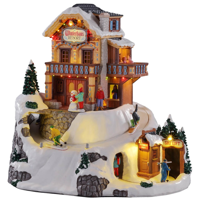 Animated, polyresin lighted building for a Lemax display. Designed to look like a rustic hotel on top of a snowy mountain. There's a person building a snowman, there's a person skiing and a person snowboarding. At the bottom of the mountain there's a person walking through an entrance to a Ski Lift.