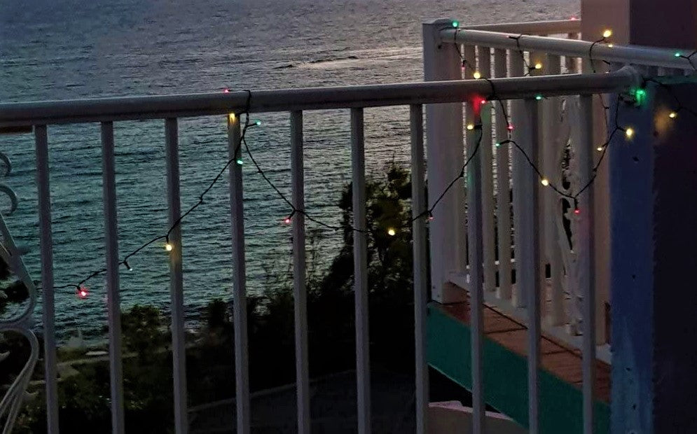 String of multi-colored LED lights hanging on a white fence overlooking a large body of water.