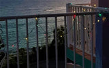 String of multi-colored LED lights hanging on a white fence overlooking a large body of water.