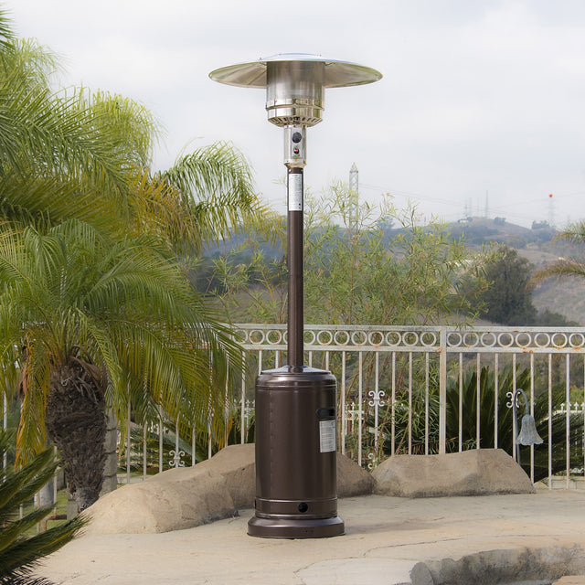 A bronze standing patio heater on a stone ledge in a fenced in backyard