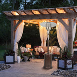 A pergola canopy on a stone patio with a cushioned outdoor patio set and a standing patio heater underneath it