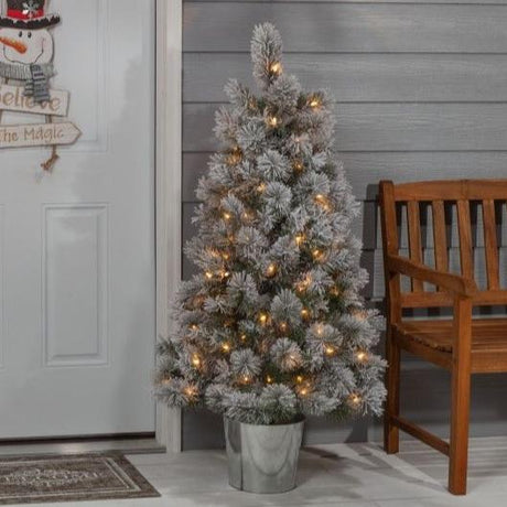 White potted artificial tree pre-lit with warm white lights. It's in a silver base.