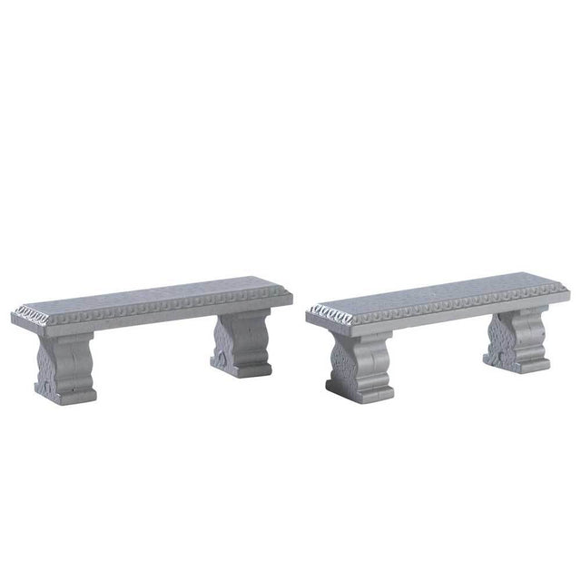 Lemax village accessories designed to look like two gray stone benches. This is a set of two. Each bench has a unique pattern around the seat and the bench's legs have a unique shape.
