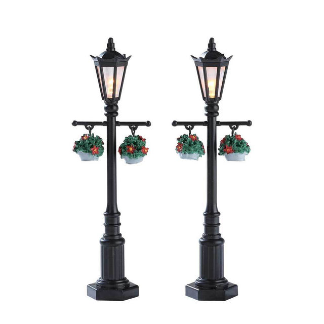 Lemax village accessories designed to look like black lampposts. There are two lampposts in this set. Each lamppost has two hanging potted plants.