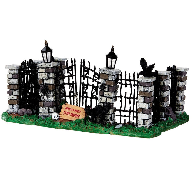 Polyresin village accent for a Lemax Spooky Town display. Designed to look like an old, worn down brick and metal fence. There are light posts on it and a black cat and a crow and a skull and a rat. There's a sign on the bottom of the fence that reads "HAUNTED HOUSE STAY AWAY!!!"