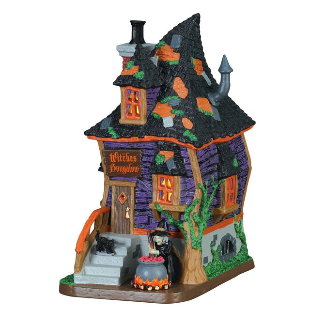 Porcelain lighted building for a Lemax display. Designed to look like a dilapidated, purple house with green vines growing up the side of it. There are holes in the roof that have been patched with green pieces of wood. There's a witch in the front stirring a cauldron and a black cat watching. 