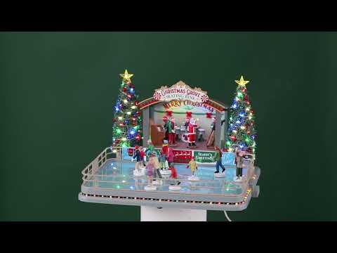 Plastic, animated figure for a Lemax display. Designed to look like an ice skating rink. There are a bunch of people skating around. There's a band on the stage in Christmas outfits and Santa hats. The sign on the stage reads "Christmas Grove Skating Rink. Merry Christmas." There are two tall, decorated Christmas trees on either side of the stage.