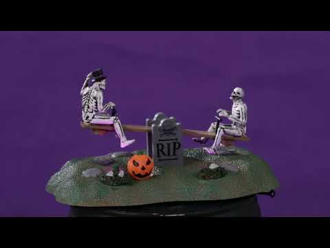 Resin village accent for a Spooky Town Lemax display. Designed to look like two skeletons on a teeter totter. One skeleton is wearing a top hat and has his leg on a carved pumpkin. There are two gravestones in the middle of the teeter totter that read RIP.