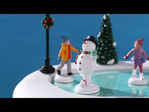 Plastic village accent for a Lemax display. Designed to look like two kids ice skating with Frosty the Snowman. There's a bench with a blue backpack on it. There are two snow-covered trees and a lamppost with a decorated wreath on it.