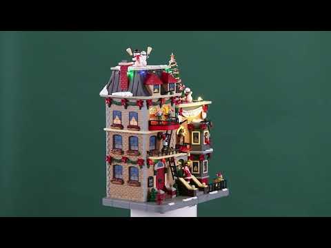 Resin lighted building for a Lemax display. Designed to look like a large, brick apartment complex that's decorated for Christmas. There are elves hanging out of the windows and standing on balconies. There are snowmen, reindeer and a decorated Christmas tree on the roof. Santa is waving from the stairs and there's a dog wearing a Santa hat on the sidewalk.